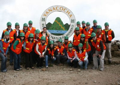 Group of people wearing hardhats in front of Yanacocha sign