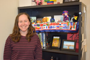 Sara Bularzik stands in front of a bookshelf featuring flags and mementos from various countries