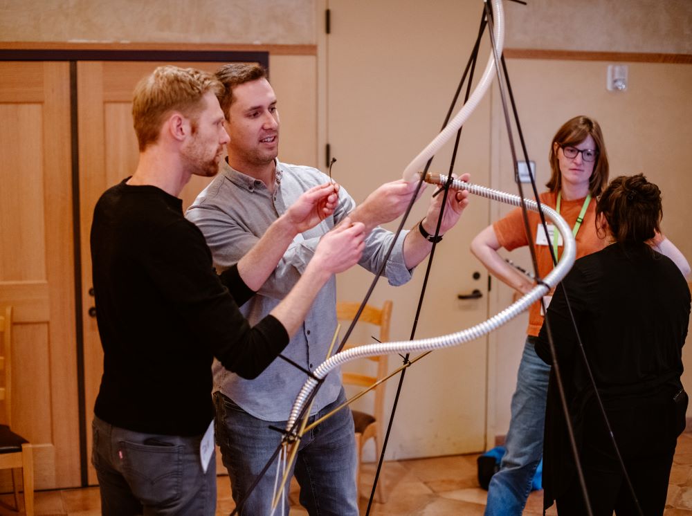 Two men weaving a plastic tube around a tripod structure